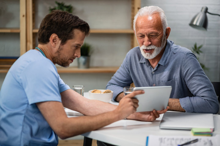 A male nurse extending a tablet to an older patient